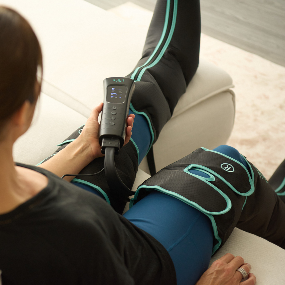 Person using a leg massager with a control device on a couch.